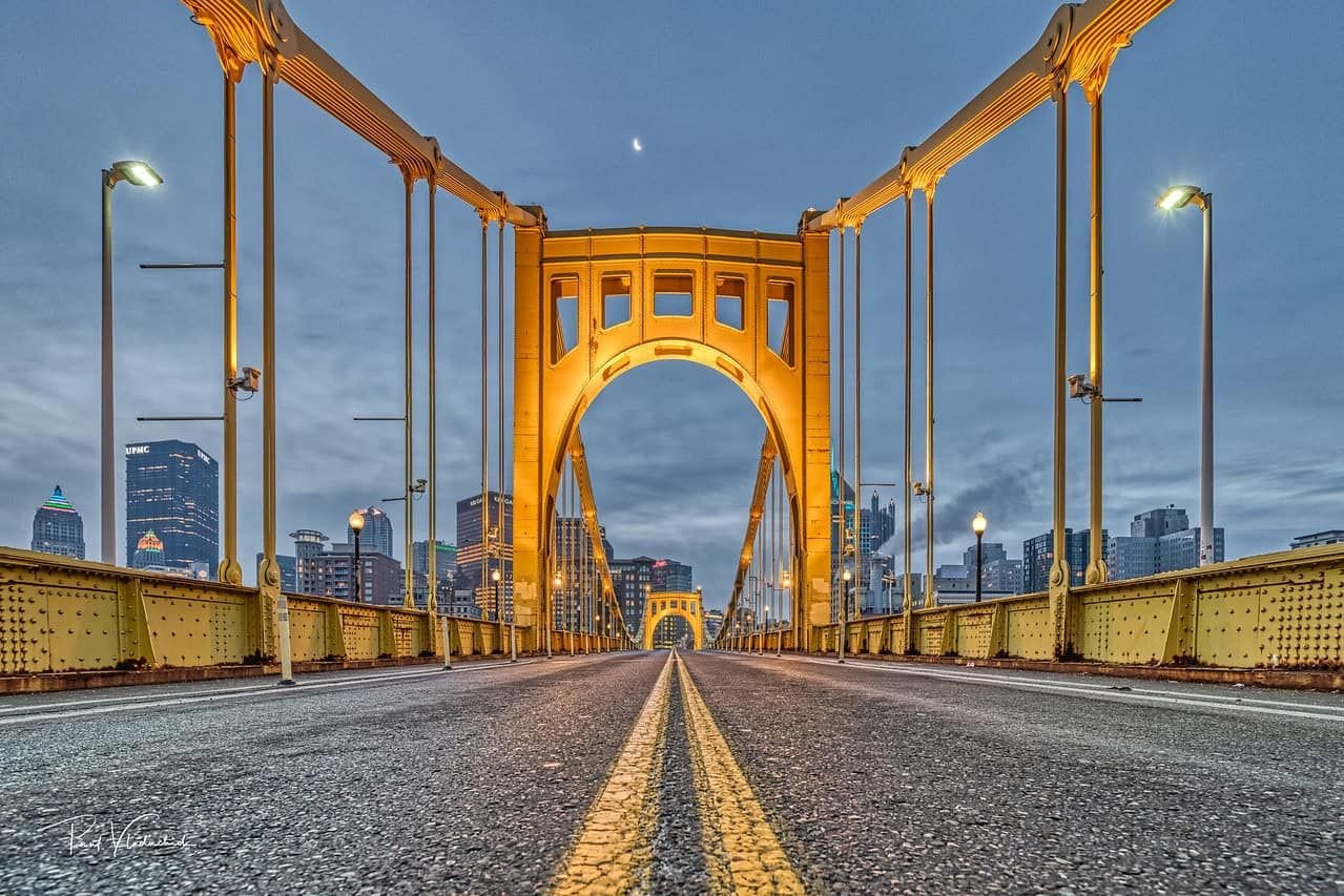 A photo of a golden bridge in Pittsburgh, lit up at night.