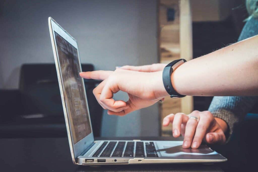 Two people are looking at a laptop screen and pointing at it.