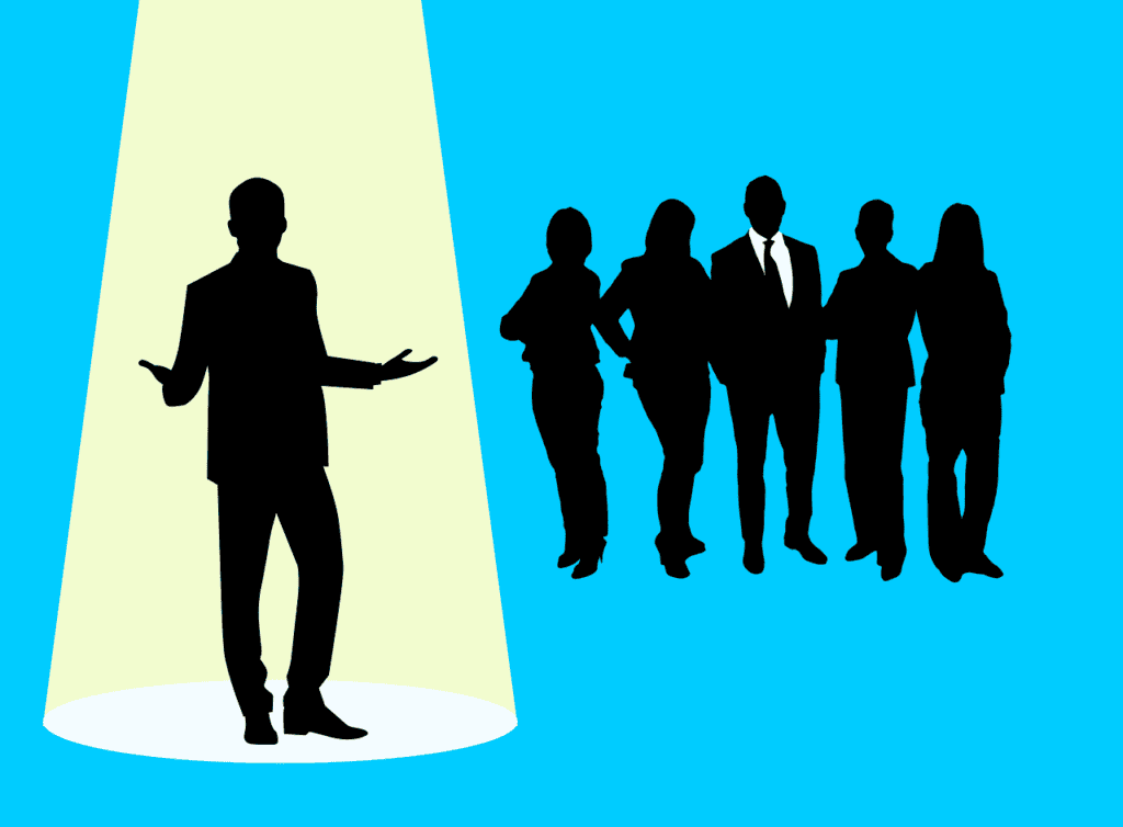 A man is in the spotlight with five other people looking at him.