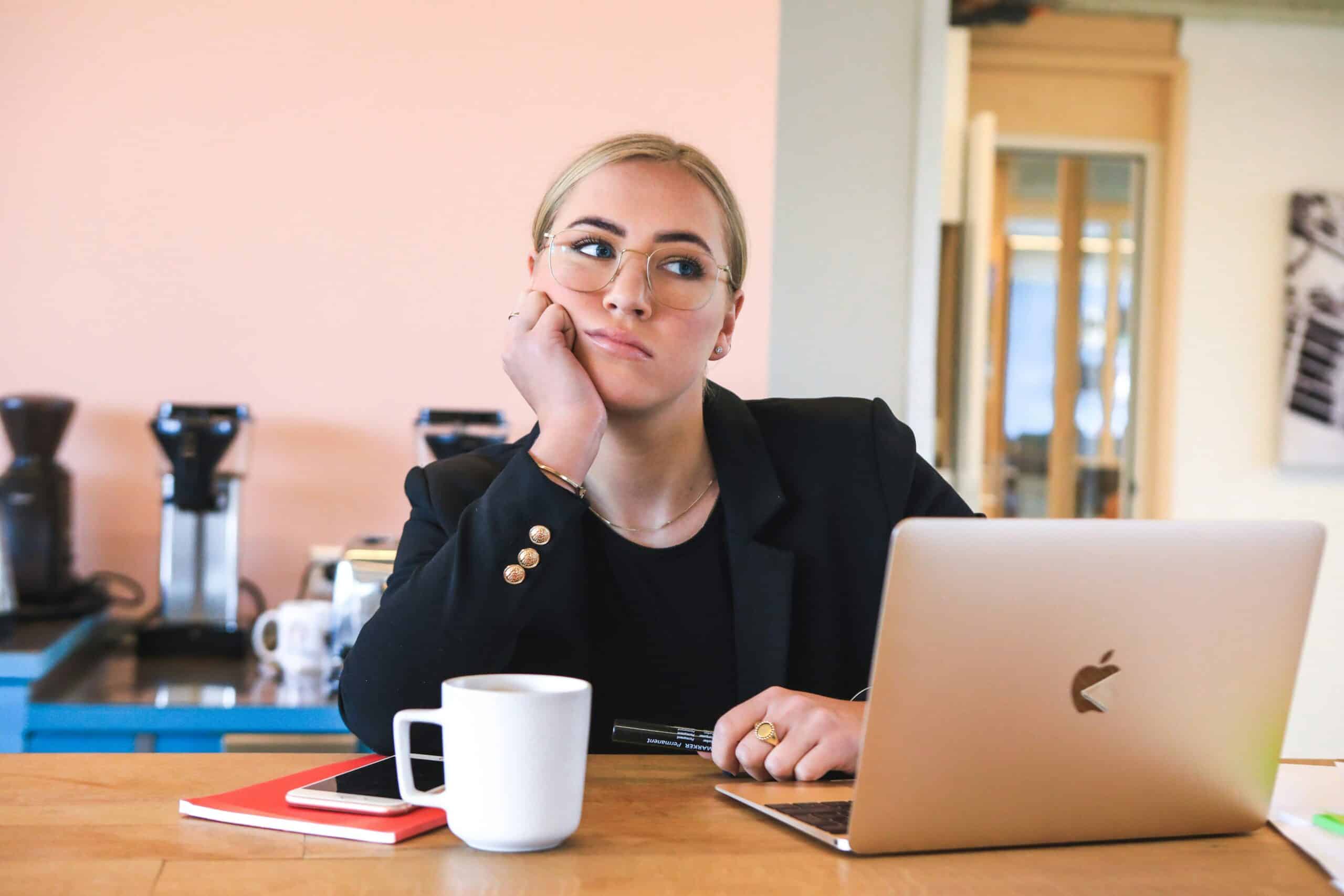 A woman at a desk with a laptop in front of her, thinking about a challenge she has.